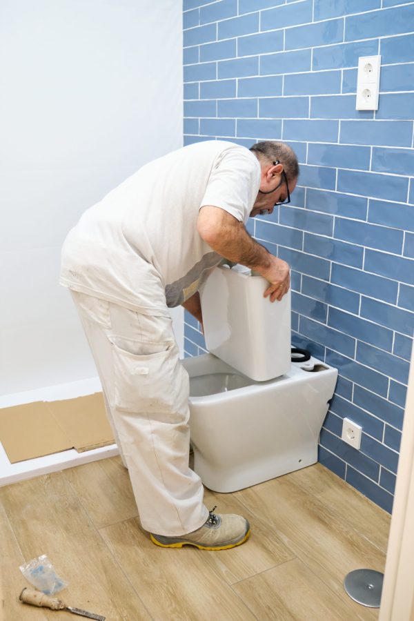 Senior plumber installer installing toilet cistern in a bathroom.